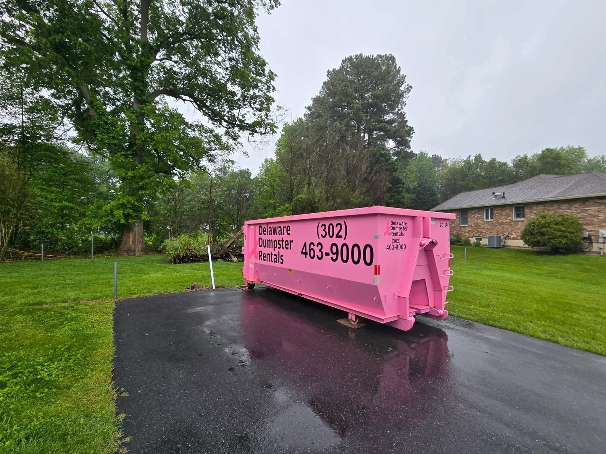 A photo of a pink Delaware Dumpster Rentals container on a residential driveway, illustrating where to start when learning how to load a dumpster rental.